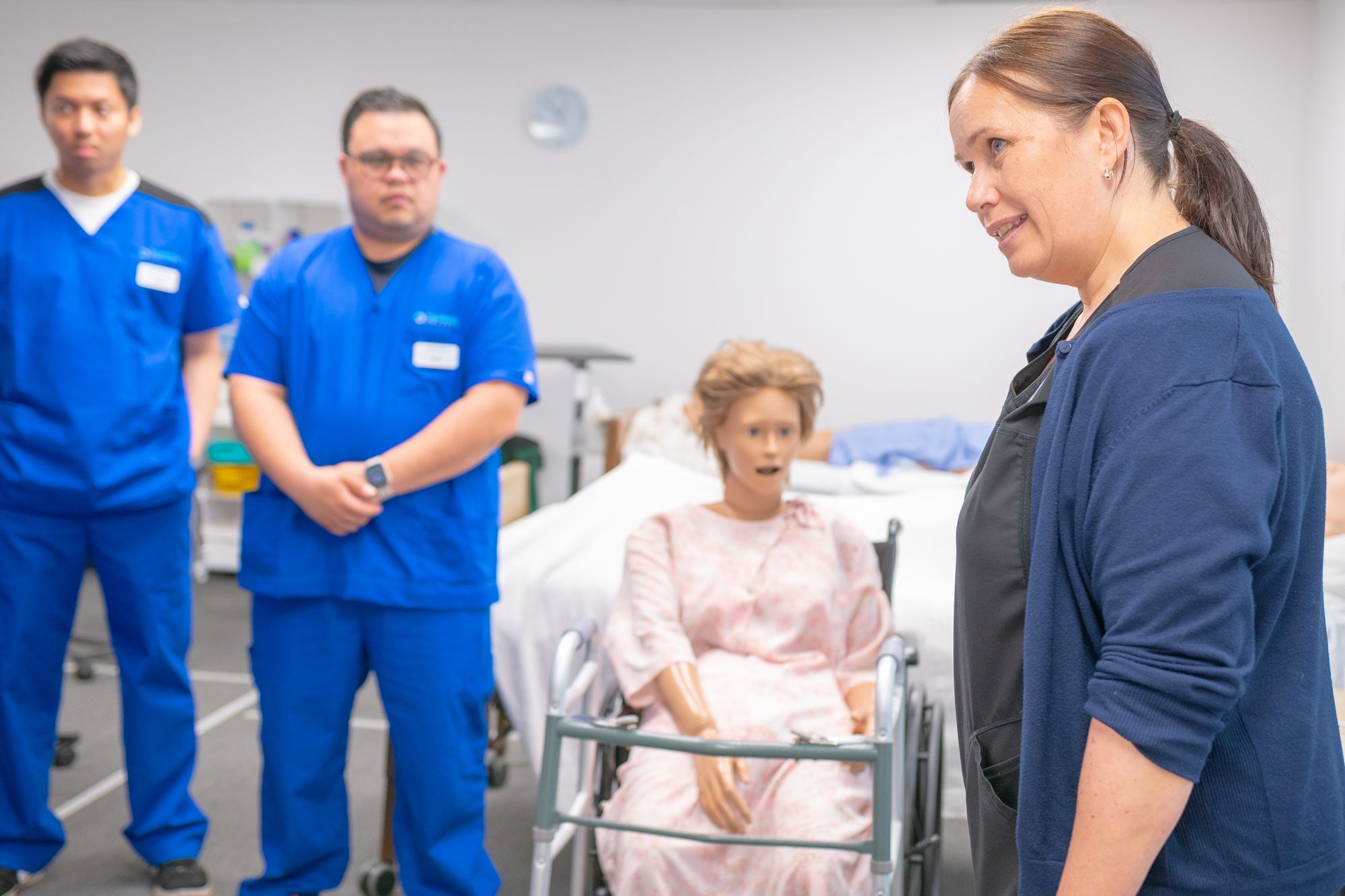 Healthcare instructor and learners beside a patient care training mannequin